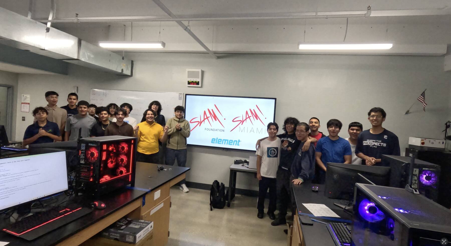 A NextBuild cohort with their finished builds, in front of SLAM Foundation and SLAM Miami screens